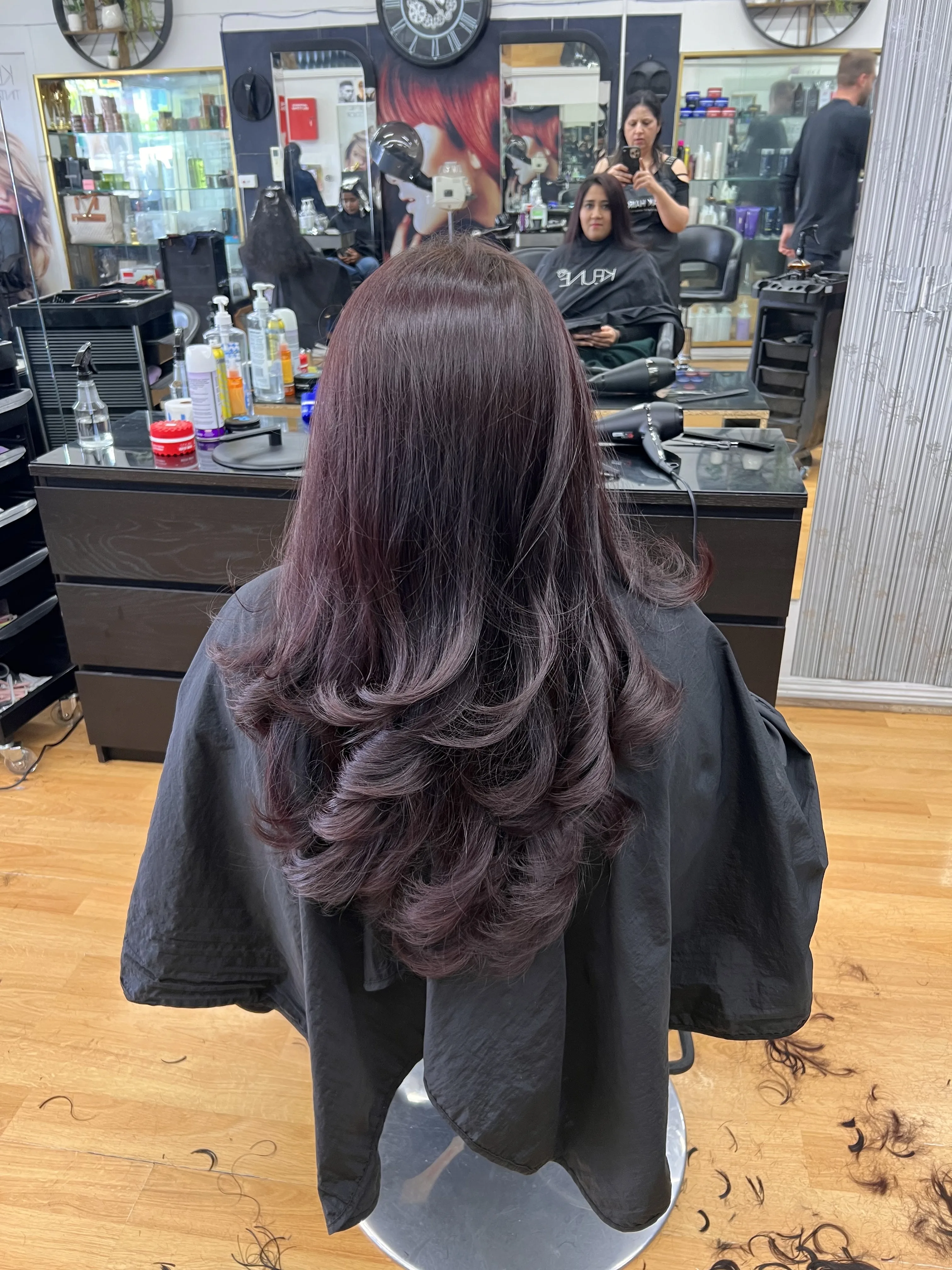 Rear view of long dark hair with soft reddish balayage, salon interior behind