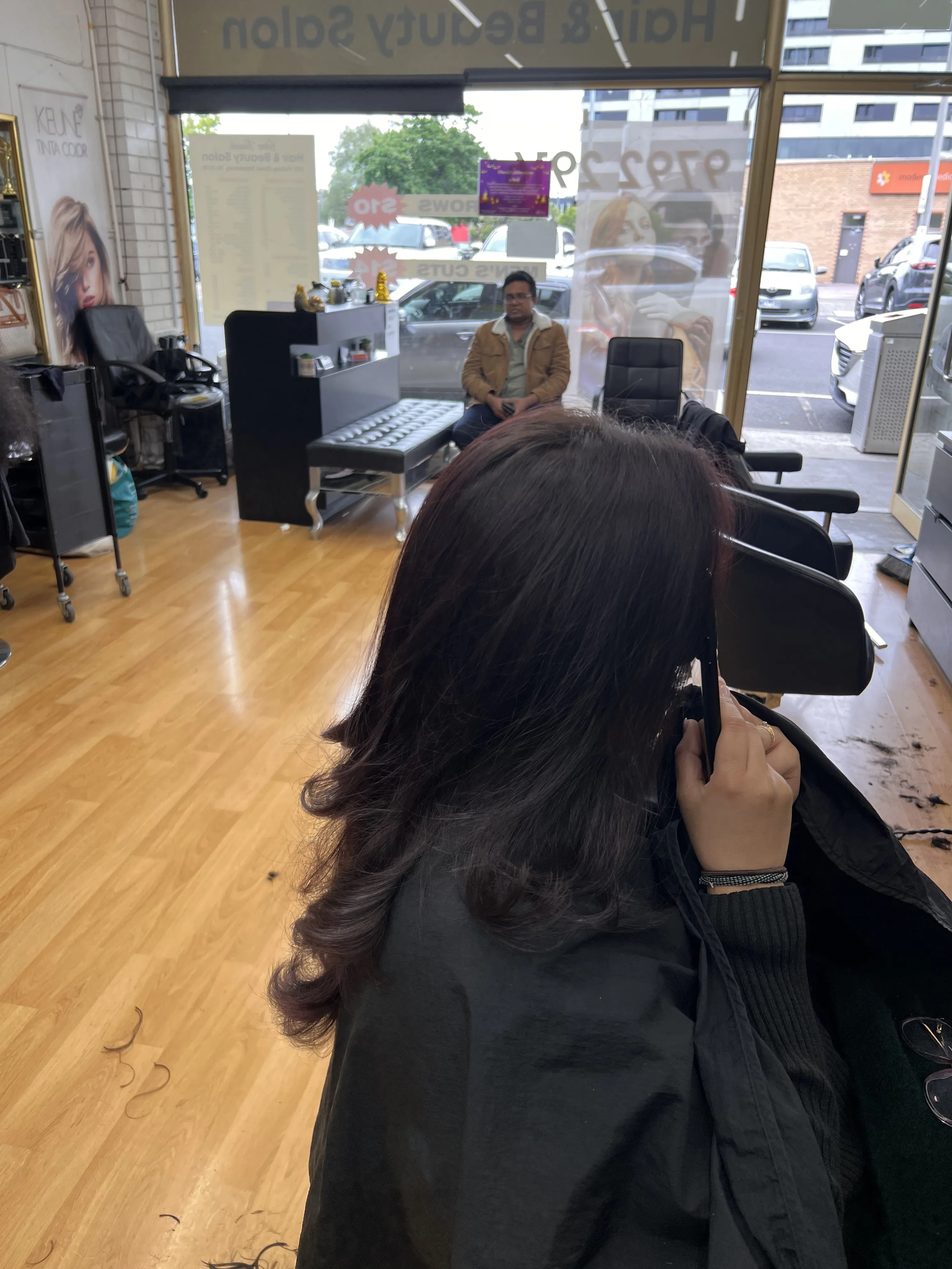 Client seated facing the street window, rear of styled hair, figure on footpath outside