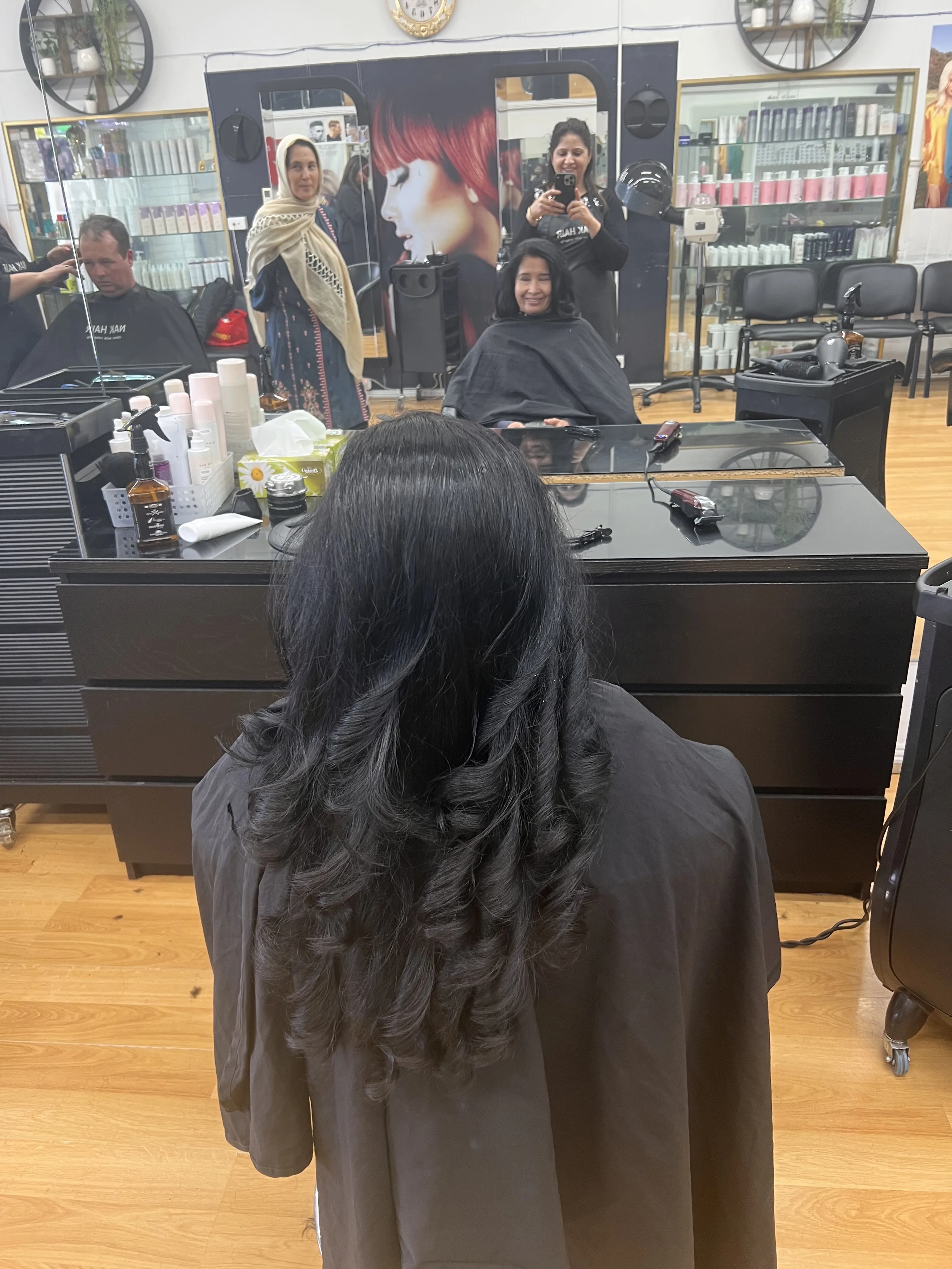 Rear view of dark wavy layered hair, staff reflections in the mirror