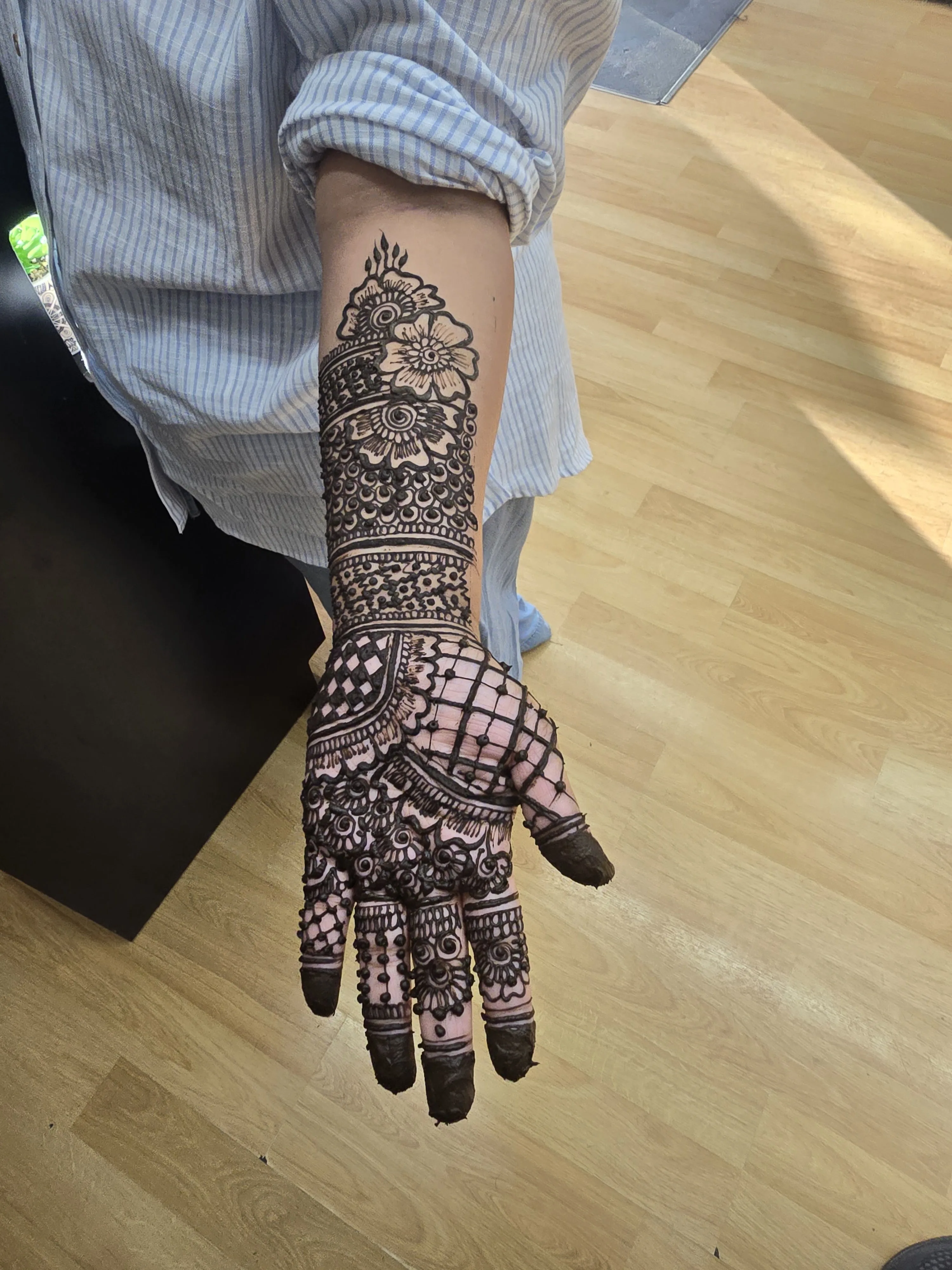 Detailed henna mehndi pattern applied across a hand and forearm on the salon floor