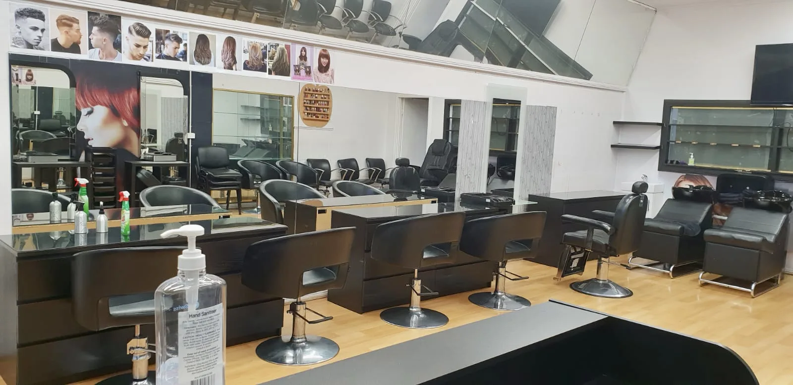 Wide interior of the salon floor showing a receding row of black leather stations, mirror wall, and backwash basins